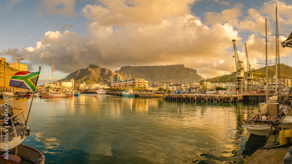 Fototapeta premium Cape Town Victoria and Alfred Waterfront port o zachodzie słońca, łódź z flagą Republiki Południowej Afryki. Table Mountain, Republika Południowej Afryki piękny krajobraz