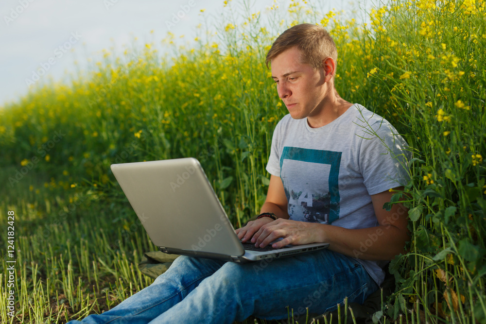 Relaxed young man using notebook on field Relaxed young man using notebook on field