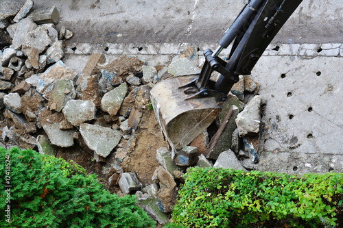 Excavator breaks and removes old concrete sidewalk. Sidewalk reconstruction.