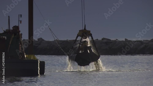 Tracking shot of industrial crane dredging in harbor