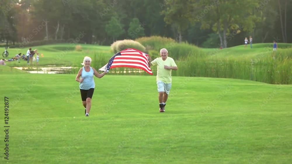 People with American flag running. Smiling senior couple outdoor. Achievments is sports. Former USA athletes. People with American flag running. Smiling senior couple outdoor. Achievments is sports. Former USA athletes.