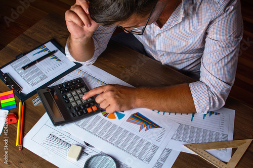 Fotografie Business analysis - calculator, sheet, graphs (business report) and analyst hand, top view