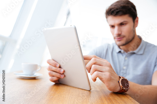 Attractive businessman in casual clothes using tablet and drinking coffee
