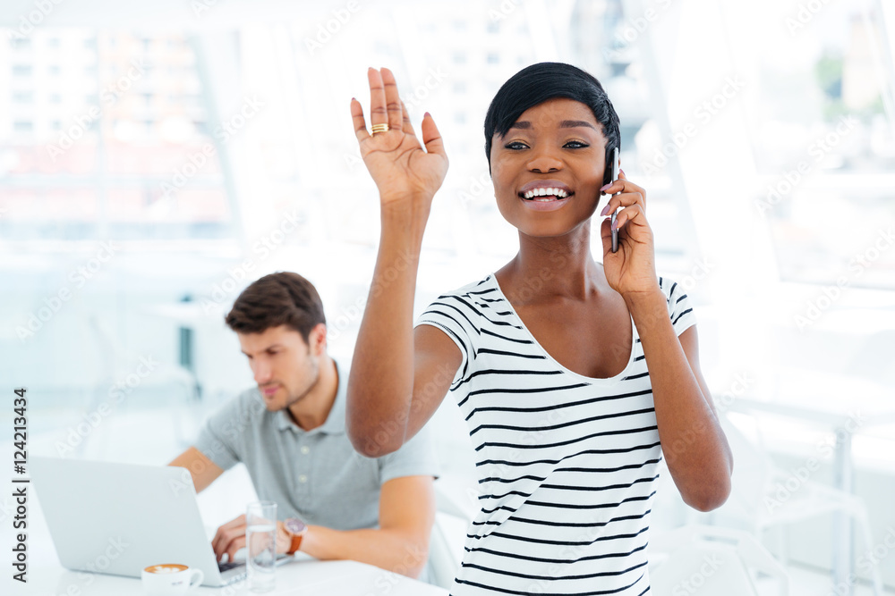 Smiling afro american businesswoman waving while talking on mobile phone