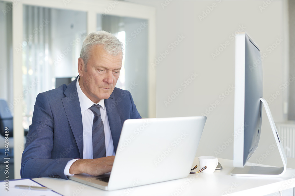 Financial businessman at work. Shot of a senior financial manager working at office in front of laptop and and doing some paperwork. Financial businessman at work. Shot of a senior financial manager working at office in front of laptop and and doing some paperwork.