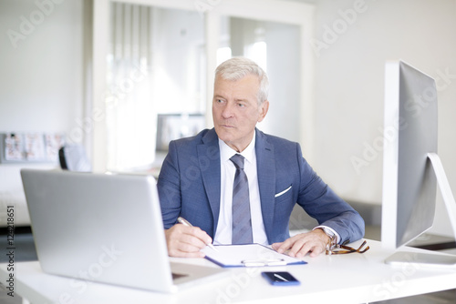 Financial businessman at work. Shot of a senior financial manager working at office in front of laptop and and doing some paperwork. 