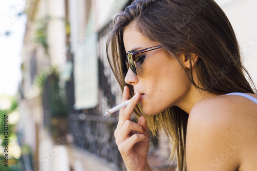 Beautiful young girl in sunglasses smoking cigarette photo