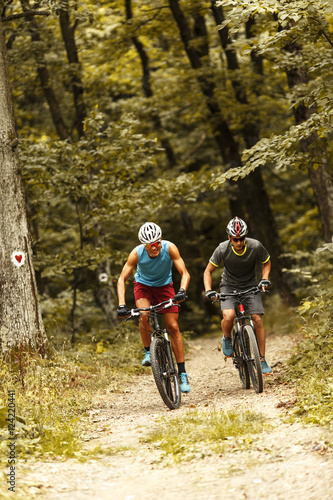 Two mountain bikers riding bike in the forest on dirt road. © BalanceFormCreative