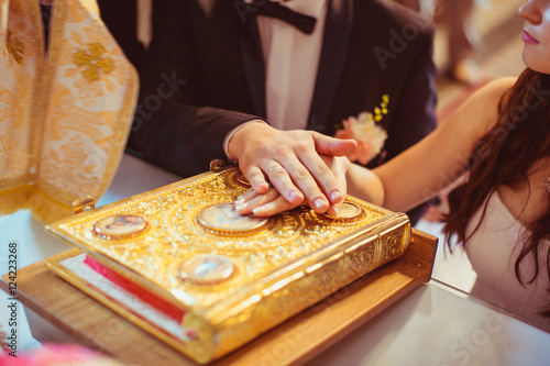 Bride and groom hold their hands over a golden Holy Bible