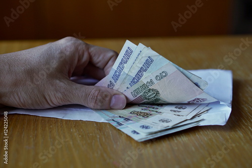 Male hand opening a white envelope full of Russian currency (Russian Ruble, RUB) on the wooden table as a symbol of cash transfer, money laundering or bribery 

in Russia