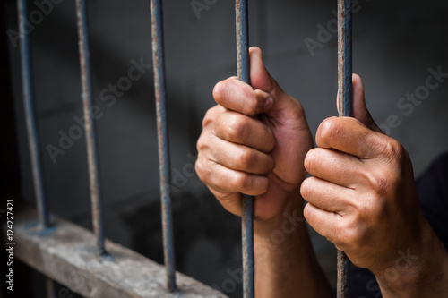 Canvas Print Soft focus on hands of man behind jail bars