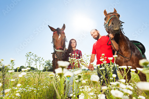 Happy couple walking with horses in summer field