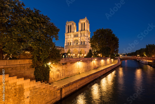 Notre Dame de Paris cathedral illuminated at twilight with the Seine River and the Pont au Double on Ile de La Cite. Summer evening in the 4th Arrondissement, Paris, France