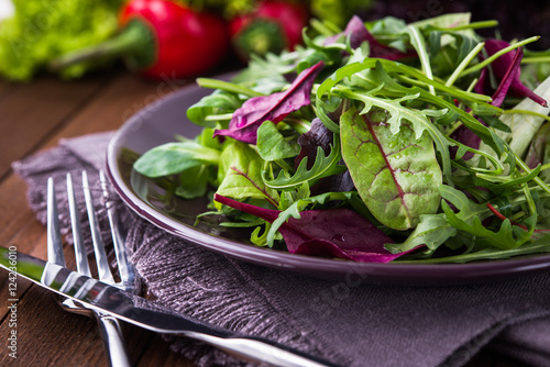 Fresh salad with mixed greens (arugula, mesclun, mache) on dark wooden background close up. Healthy food.