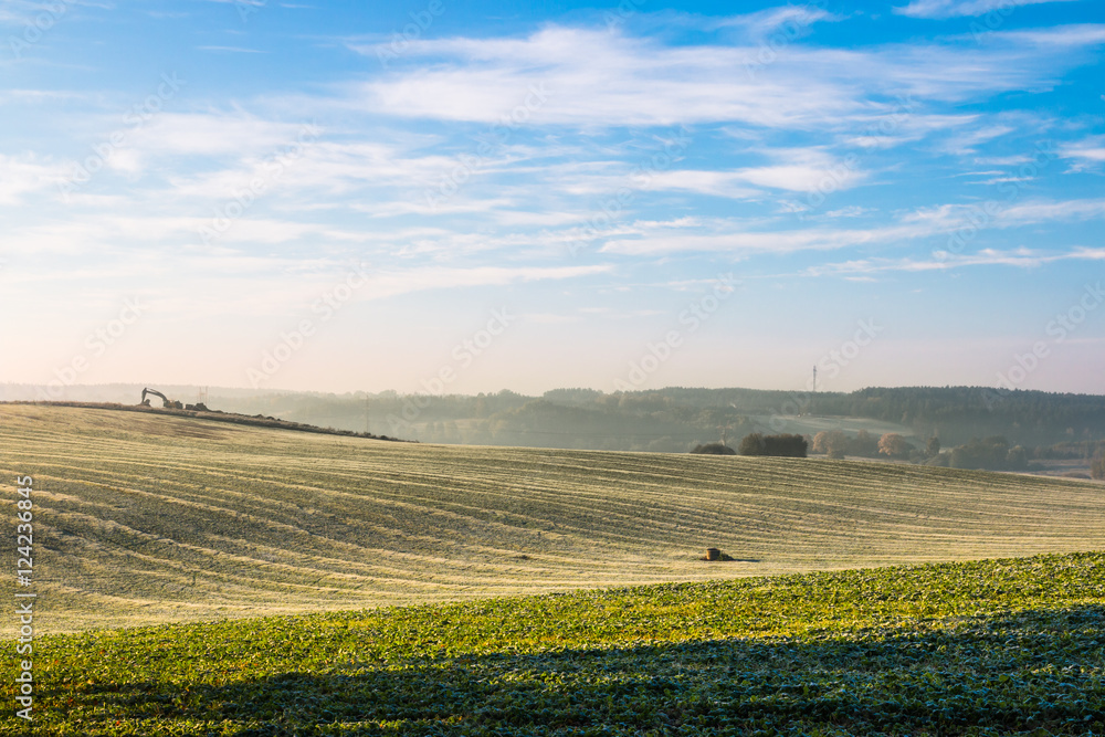 The first frost in the fields. Misty autumn morning. On the horizon the area of road investments.
