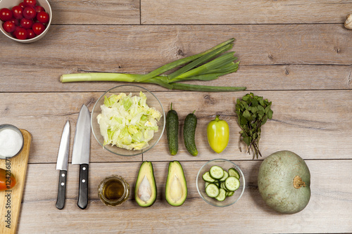 High Angle Still Life View of Knife and Wooden Cutting Board Surrounded by Fresh Herbs. Assortment of Raw Vegetables on Rustic Wood Table