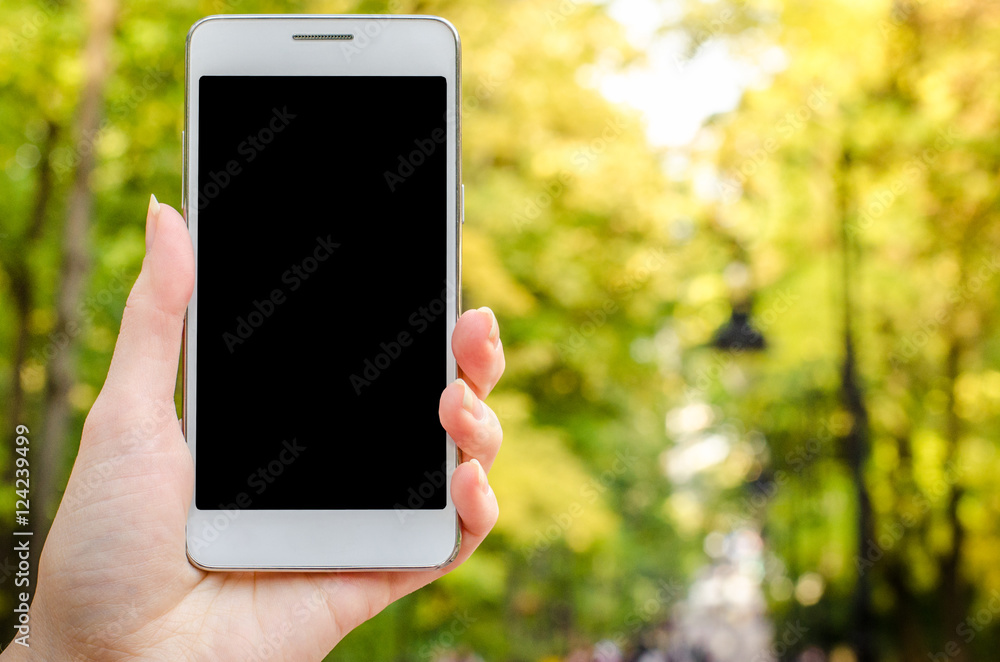 close up white mobile phone in hand a young hipster business woman on the background of green natural  grass and autumn leaves 