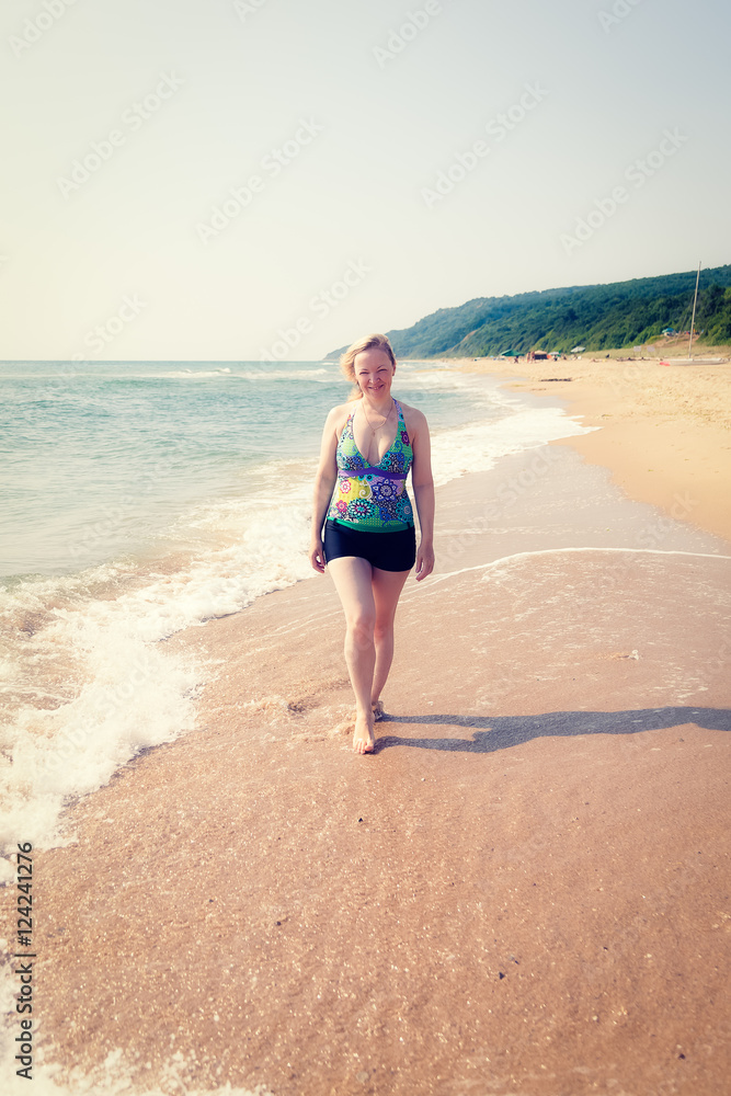 A woman walks on the sandy beach in a bathing suit