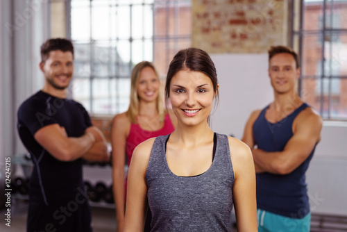 lächelnde junge frau im fitnessstudio mit freunden hinter ihr