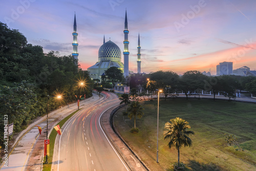 View of Shah Alam Mosque with blue skies and white clouds during sunrise.