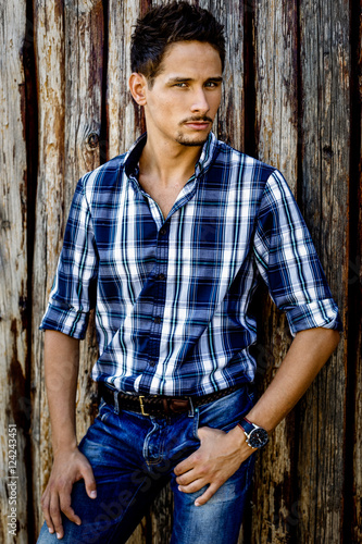 handsome young man in blue shirt standing near wooden wall