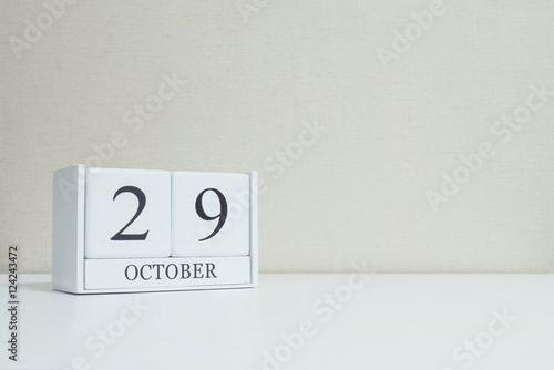 Closeup white wooden calendar with black 29 october word on blurred white wood desk and cream color wallpaper in room textured background with copy space , selective focus at the calendar