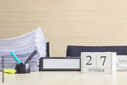 Closeup white wooden calendar with black 27 october word on blurred brown wood desk and wood wall textured background in office room view with copy space , selective focus at the calendar