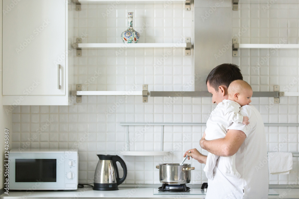 Man in the kitchen holding a child on his shoulder, cooking in the pan. New born, bonding concept photo, family Man in the kitchen holding a child on his shoulder, cooking in the pan. New born, bonding concept photo, family