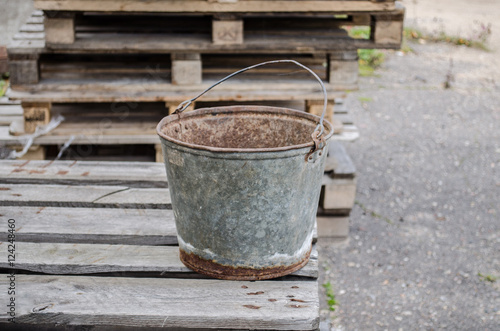 an old iron bucket in the garden at wooden pallet / an old rusty bucket / Old galvanised bucket /