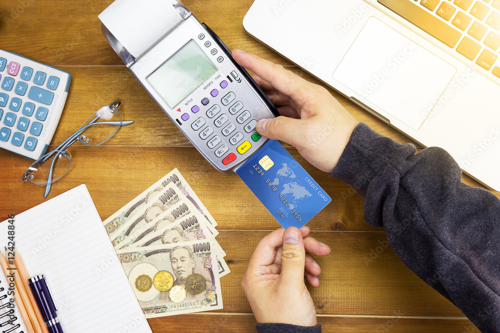 Φωτογραφία Cashier hand holding a Credit card over EDC machine or credit card terminal with calculator and glasses