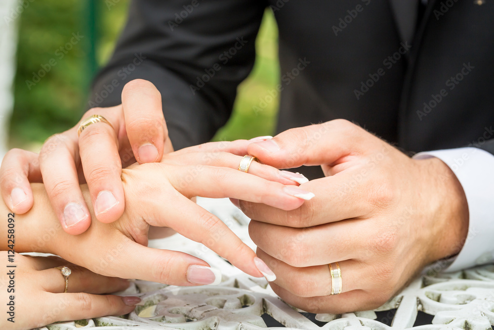Fototapeta premium Groom putting a wedding ring on bride's finger in outside