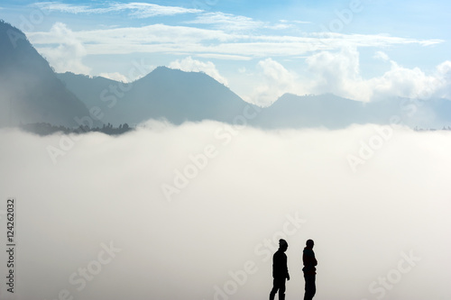 Silhouette of two horsemen resting on the sand dune with foggy / misty morning background at Bromo-Tengger-Semeru National Park, East Java, Indonesia