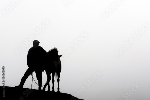 Silhouette of a horsemen resting on the sand dune with foggy / misty morning background at Bromo-Tengger-Semeru National Park, East Java, Indonesia