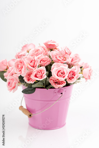 Romantic decor of pink and white, yellow, cream rose flower bouquet in the pink and blue iron (metal) bucket/container. Isolated background.  Greeting card with artificial flowers.