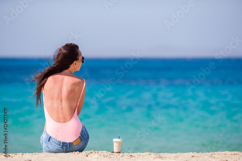 Young beautiful woman on the beach during tropical vacation. Girl drink cold coffee on one of the beautiful beaches in Mykonos, Greece, Europe.