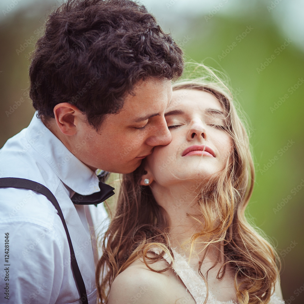 Tender man kisses woman's peach cheek while wind blows her hair Tender man kisses woman's peach cheek while wind blows her hair