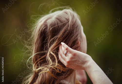 Tender woman's hand with a ring adjusts curly hair