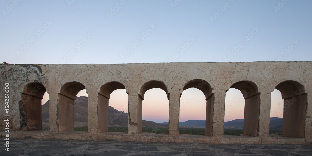 A structure with arches in a row and hills in the background at sunset A structure with arches in a row and hills in the background at sunset