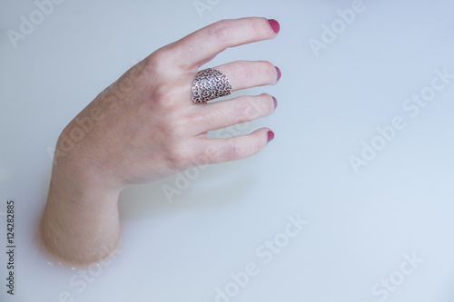 A girl's hand protruding from a bath of water and milk in a bathtub. The rest of the body is submerged. The photo has an artistic touch. 