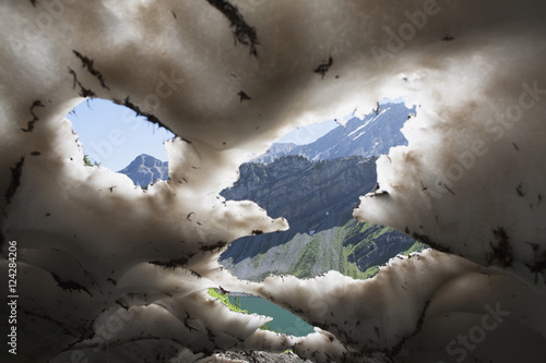 Underneath a melting snow pack with gaps showing mountains and lake with blue sky in kananaskis provincial park;Alberta canada photo