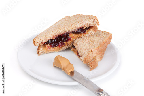 Peanut Butter and Jelly Sandwich – A peanut butter and grape jelly sandwich. On a white plate, on a white background. Knife with peanut butter in the foreground.