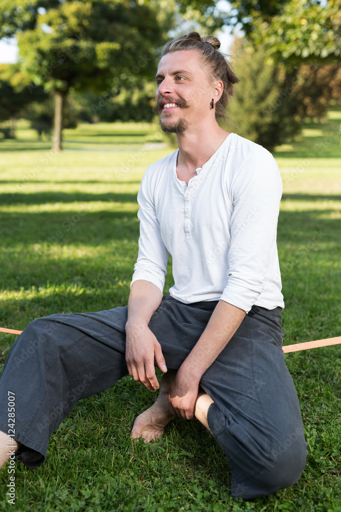 Fototapeta premium portrait of man sitting on slackline and balancing on a rope