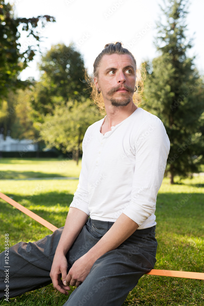 portrait of man sitting on slackline and balancing on a rope portrait of man sitting on slackline and balancing on a rope