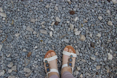 Female feet in sandals on gravel background.