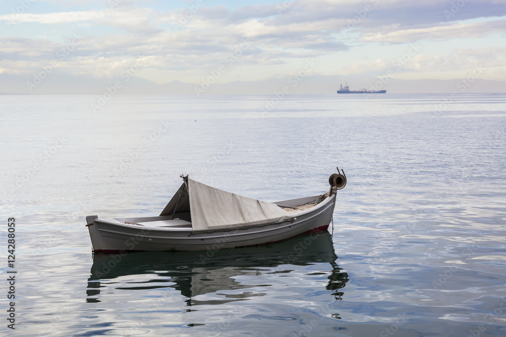 A boat floating on the tranquil Aegean Sea with a ship in the distance; Thessaloniki, Greece A boat floating on the tranquil Aegean Sea with a ship in the distance; Thessaloniki, Greece