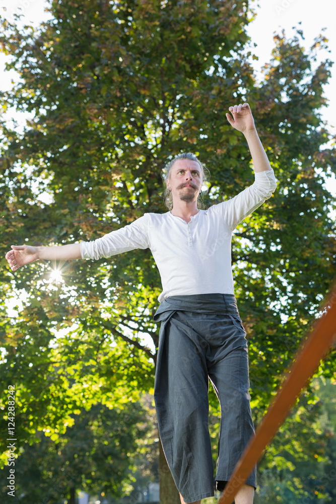 Man walking barefoot on slackline in park with arms out and deep