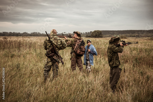 Hunting scene with hunters aiming during hunting season in rural field in overcast day with moody sky 