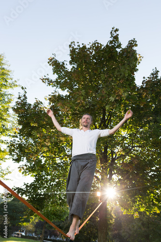 Man walking barefoot on slackline in park with arms out