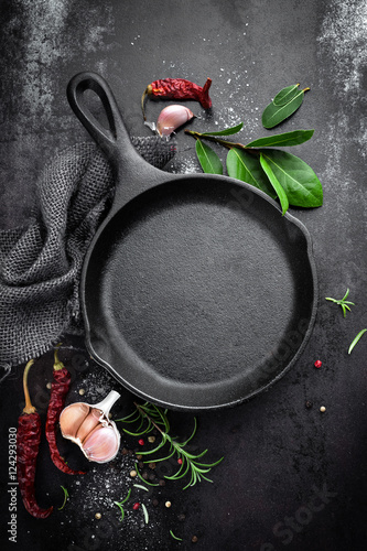 cast iron pan and spices on black metal culinary background, view from above
