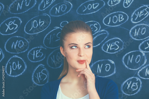 Young woman is standing on blackboard background and thinking: yes or no.